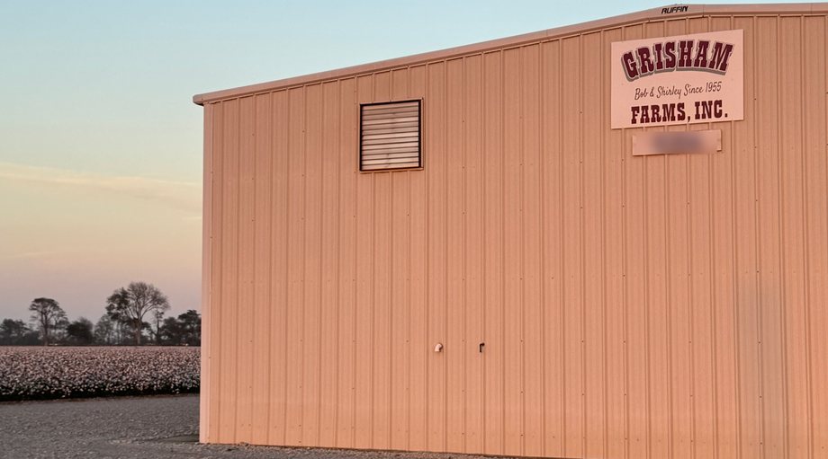 The Grisham Farms shop at Black Oak at sundown, a field of open cotton beyond it. Its sign reads Grisham, Bob and Shirley since 1955, Farms, Inc.